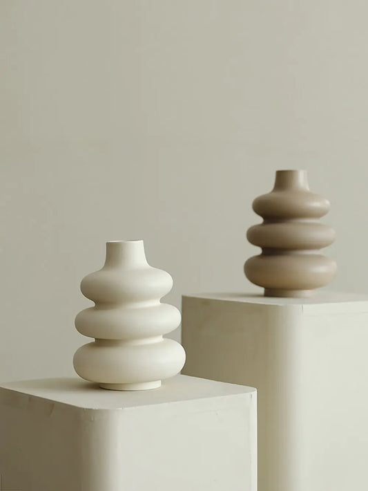 Two ceramic vases, one white and one brown, on a neutral background