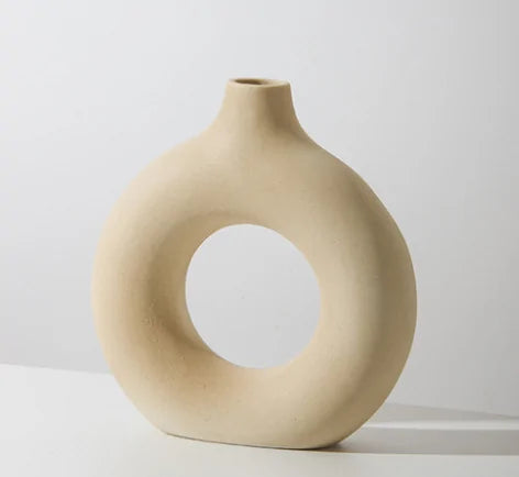 Beige ceramic vase with a circular hole on a light gray background